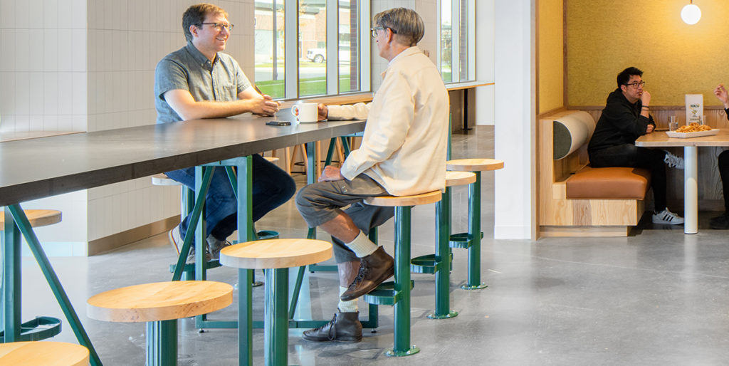Employees sitting on green Sally Bolt Down Stools with natural wood seats.
