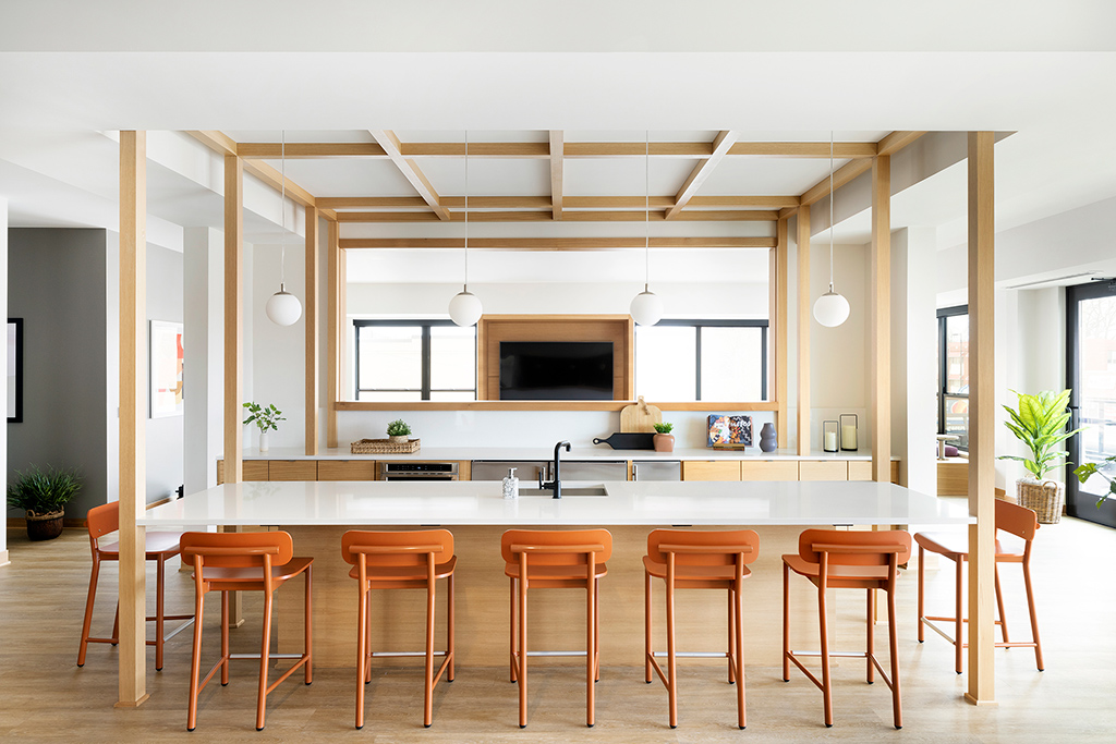 Monochromatic orange stools along a communal kitchen in a multi-family development.